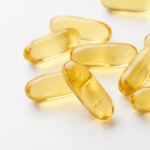 A collection of translucent yellow softgel capsules scattered on a plain white background.