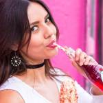 Woman drinking soda from a glass bottle, highlighting the impact of soft drinks on dental health and enamel erosion