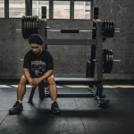 Man sitting in a gym looking thoughtful, reflecting on muscle building tips and workout mistakes