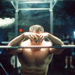 Man resting in gym after intense workout, showing muscle fatigue and recovery phase after strength training