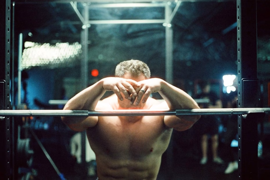 Man resting in gym after intense workout, showing muscle fatigue and recovery phase after strength training