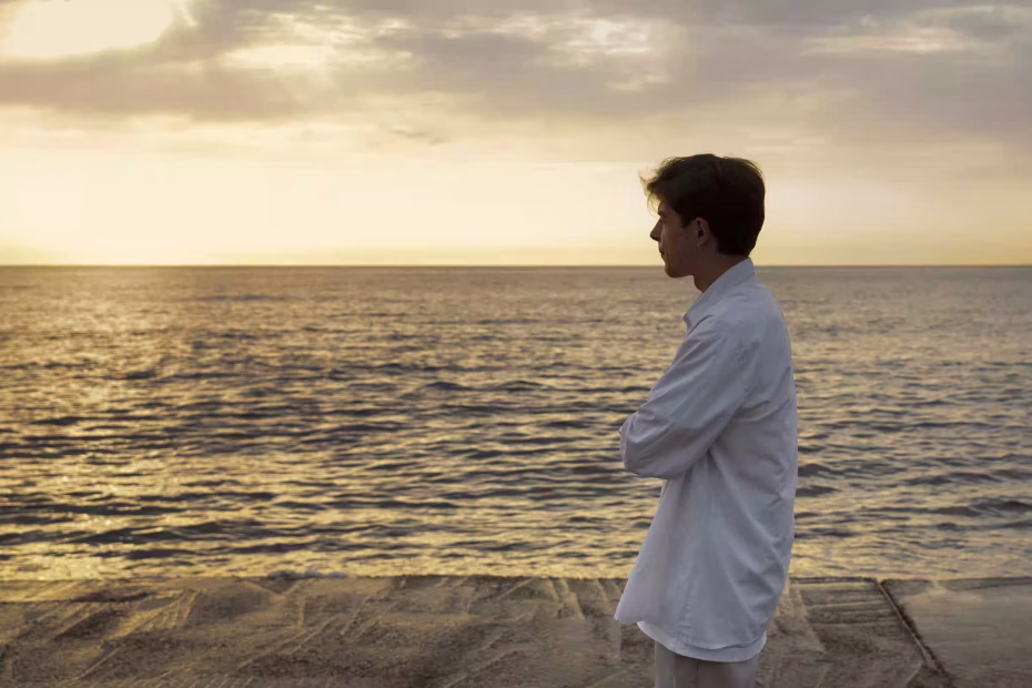 A stressed man standing by the sea, looking into the distance, seeking calm and mental clarity.